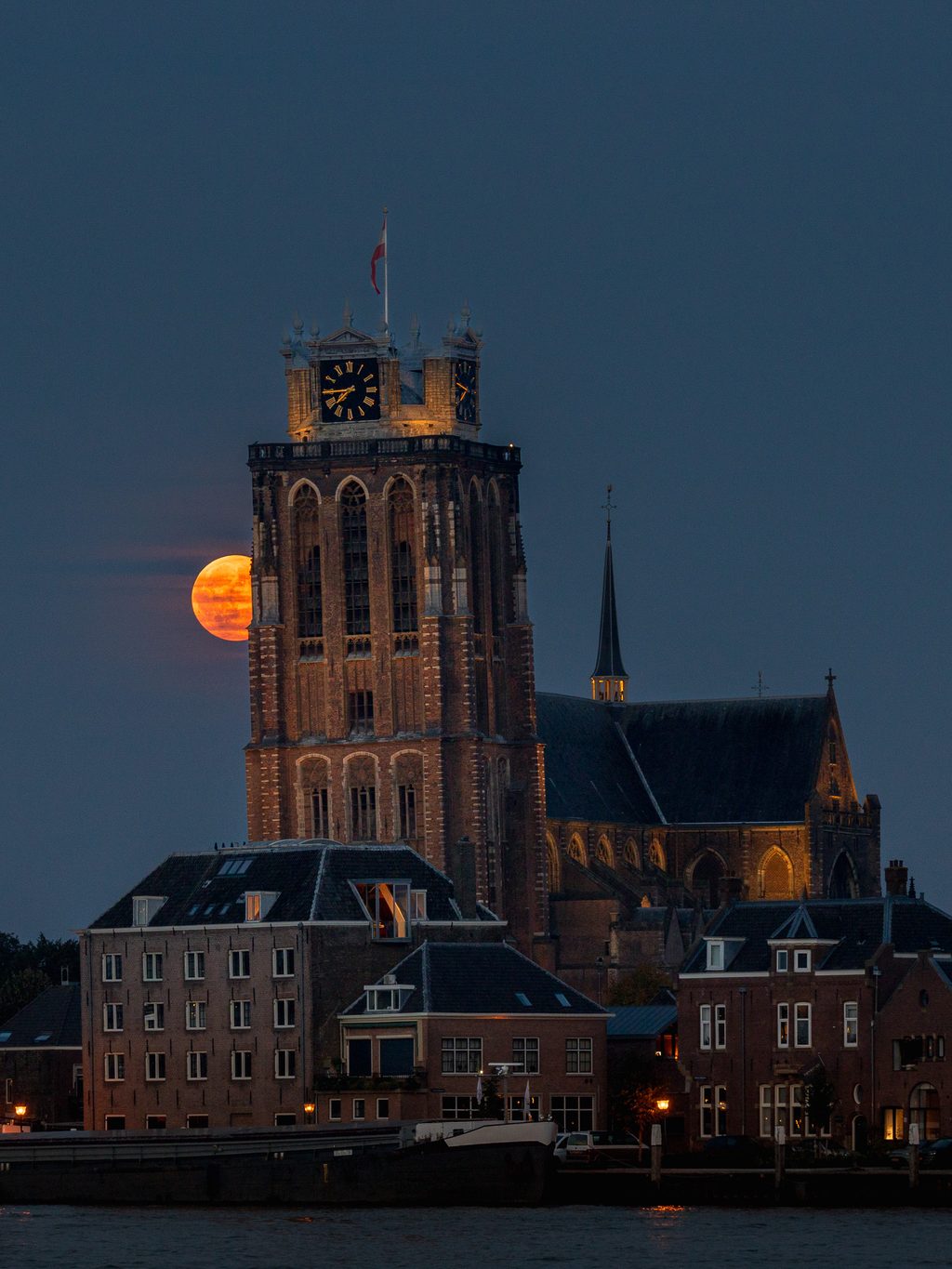 De oranje volle maan half verscholen achter de toren van de Grote Kerk