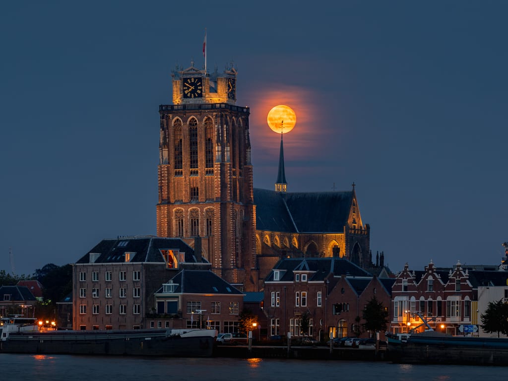 De volle maan direct achter de windhaan op de spits van de Grote Kerk