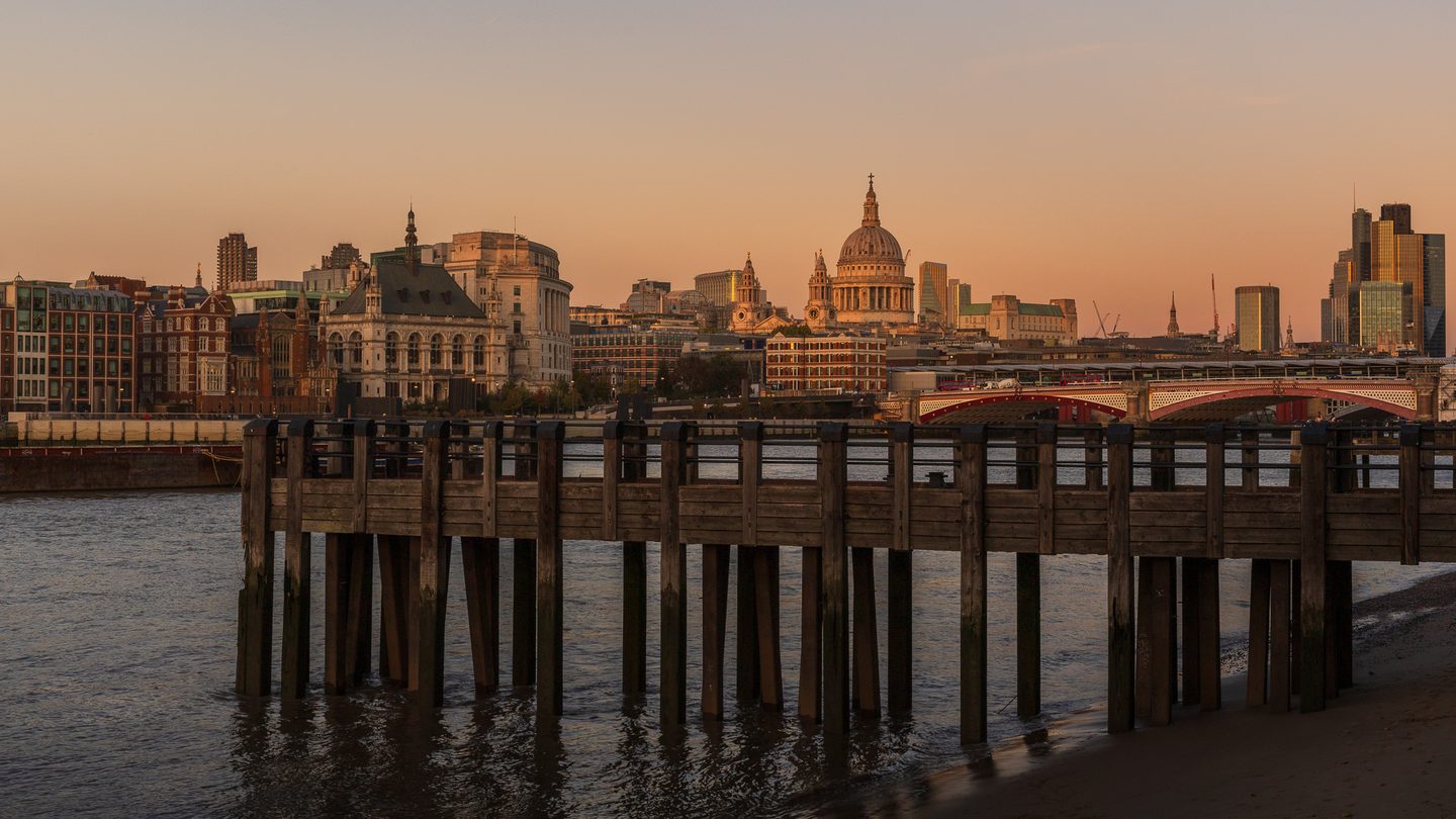 St Paul's Cathedral and the City skyline at sunset, seen across the Thames from a wooden pier