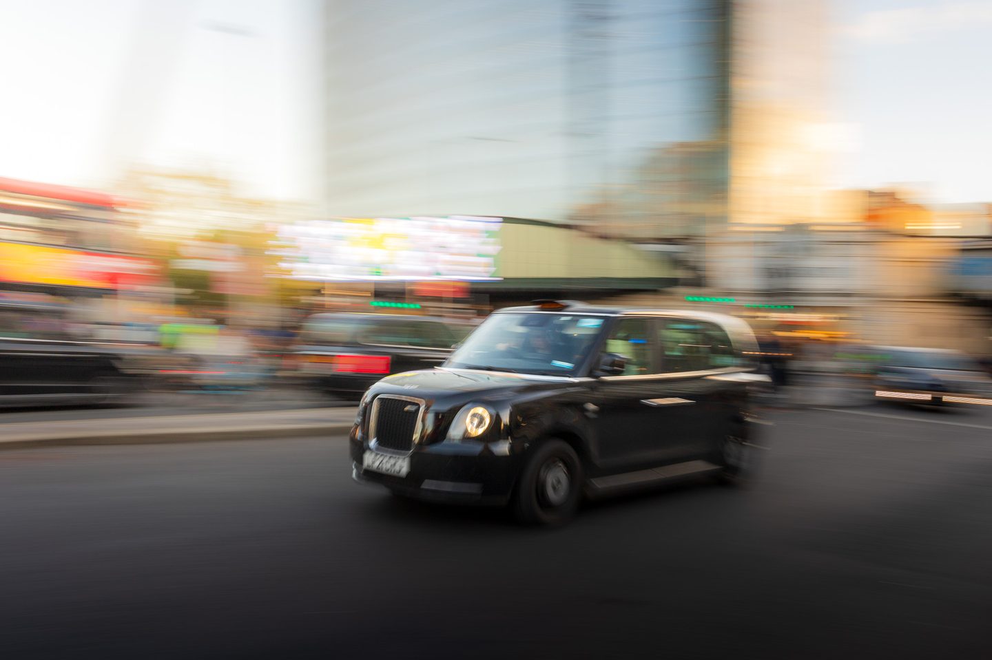 A black London taxi speeding through a blurred city street